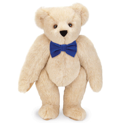 Honey-colored plush teddy bear with brown eyes wearing a royal blue bow tie.
